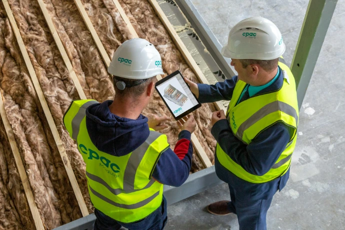 Two construction workers review plans on a tablet.